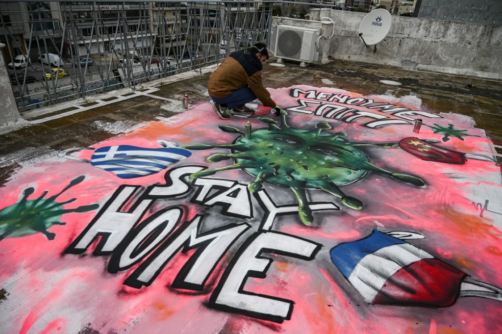 Artist S.F. paints a mural about the COVID-19 crisis on the roof of his building in Athens. Image