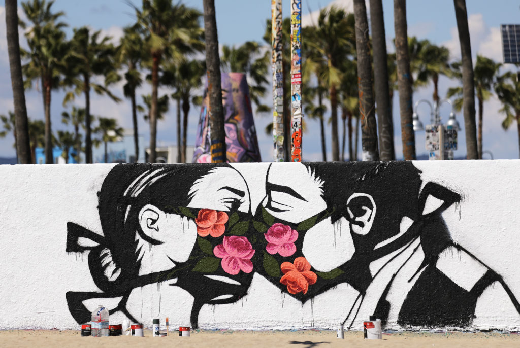 A coronavirus street art work by Pony Wave depicting two people kissing while wearing face masks on Venice Beach. Photo by Mario Tama/Getty Images. Image
